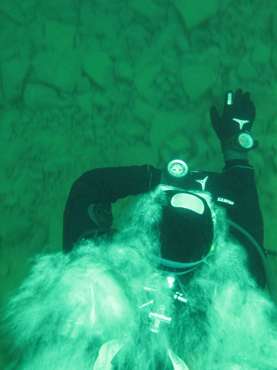 Top-down view of a scuba diver checking a wrist compass above a rocky bottom in green water